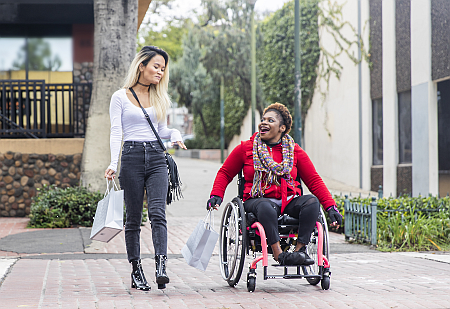 Two woman, one in a wheelchair, crossing the street